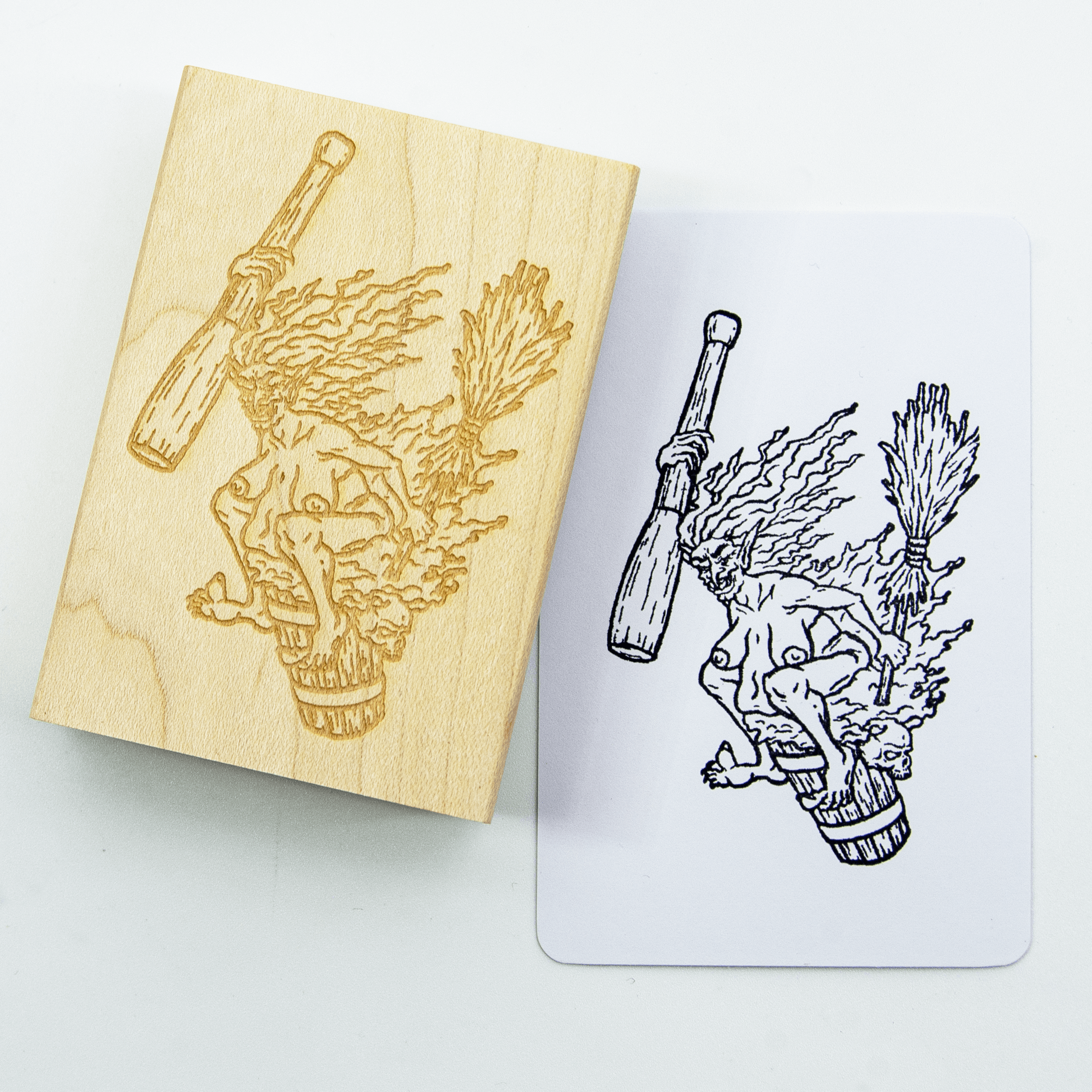 A wood and rubber stamp of Baba Yaga the crone witch, riding her mortar and pestle with broom in hand. She has taken off her clothing and sits on it with a wicked smile. A stamped white notecard shows the design in black ink.