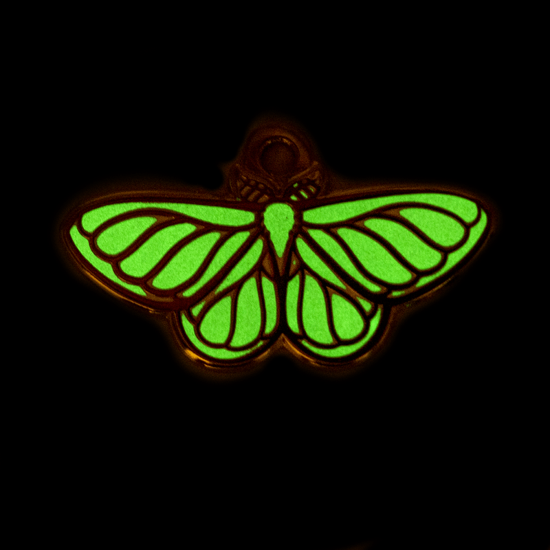 A small enamel moth charm glowing green in the dark.