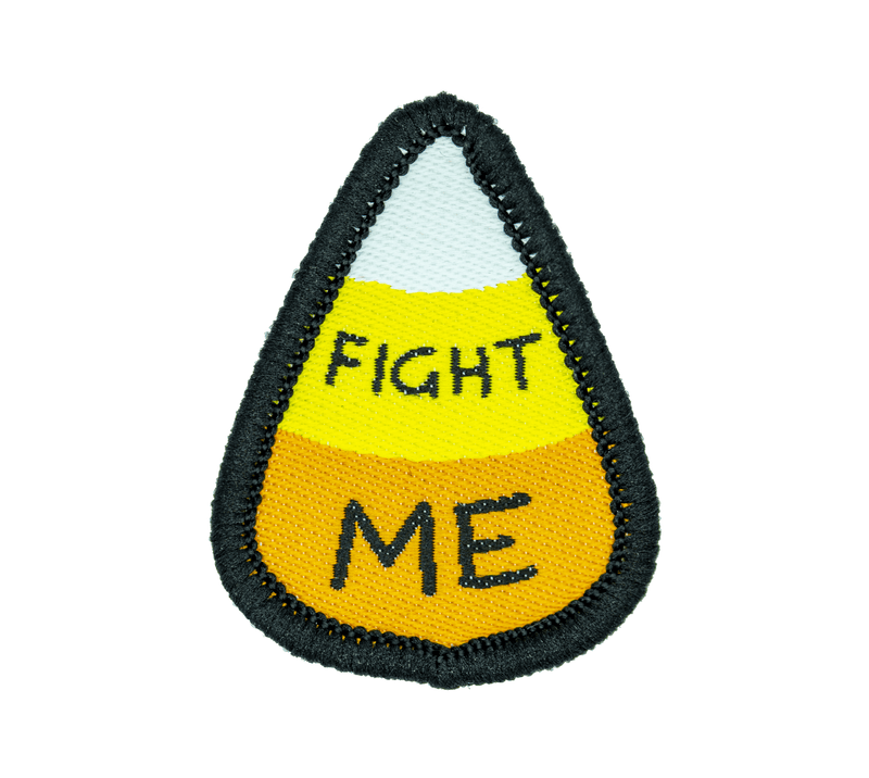 A small woven patch in the shape of a white, yellow, and orange candy corn, with black text reading "FIGHT ME".
