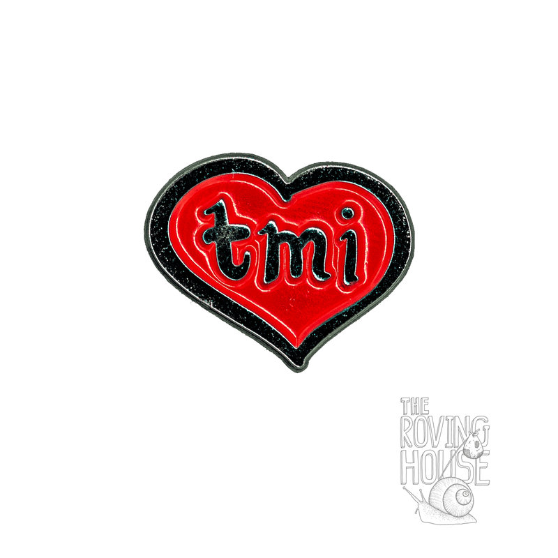 An enamel pin of a red heart with the text "tmi" written inside it.