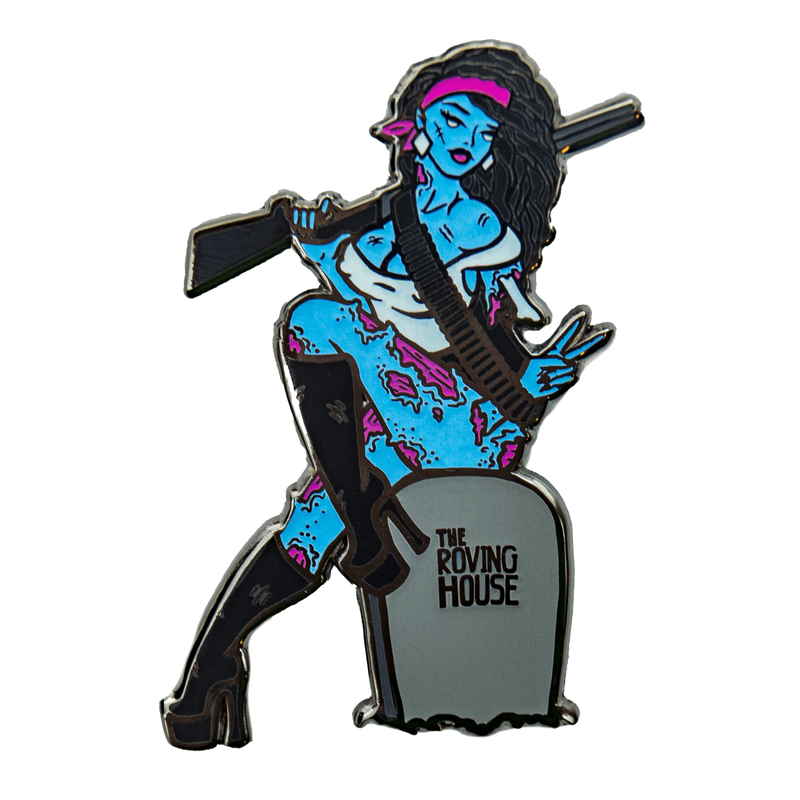 An enamel pin of a beautiful, buxom, blue zombie woman sitting atop a gravestone. Her right arm holds a shotgun over her shoulder. Her left arm has been torn off, but her hand is tucked inside her ammo belt and gives the peace sign.