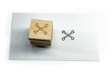 A wood and rubber stamp of crossbones, next to its inked stamped artwork.