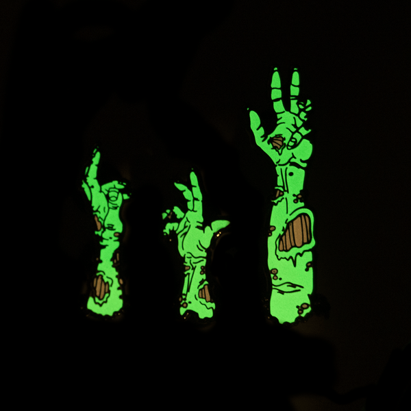 A set of three zombie arm pins, glowing in the dark.