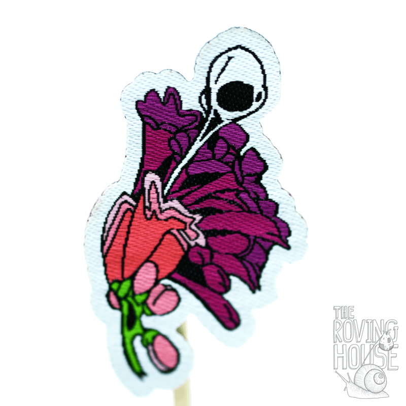 A small woven patch of a hummingbird skull sipping from some blossoms.