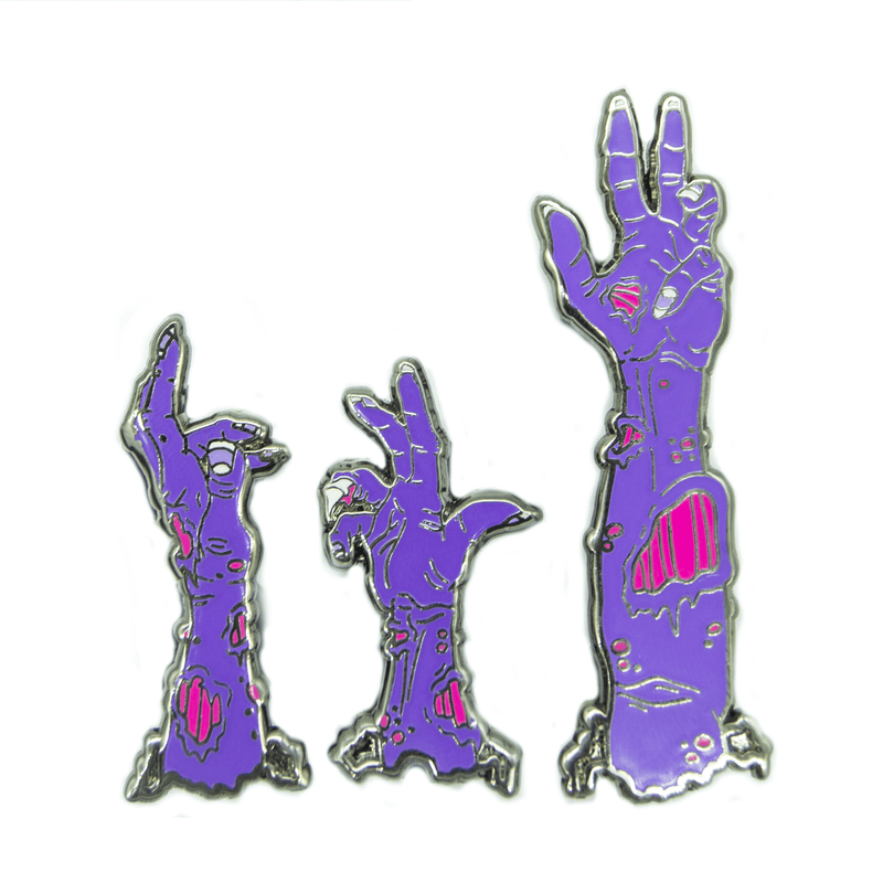 A set of three zombie arm pins, appearing to come up from the ground. Their skin is purple, and their flesh wounds are neon pink.