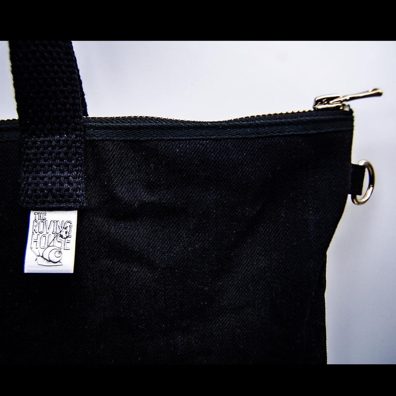 A closeup of the Rover Ita Pin Tote, showing the Roving House snail logo on a tag, a heavy-duty zipper, and a D-ring for holding keys.