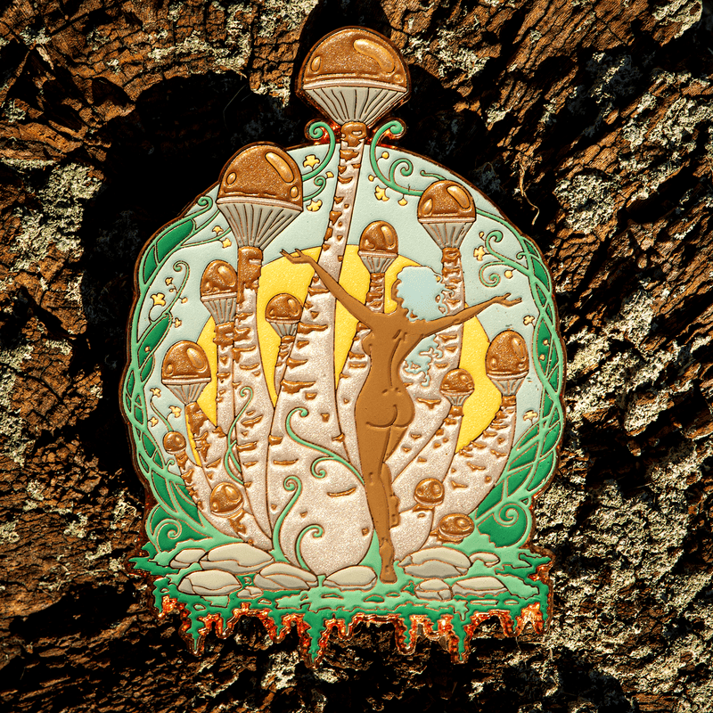 A large enamel pin of a nude, blue-haired woman dancing in front of giant mushrooms with pearlescent browns, blues, and greens.