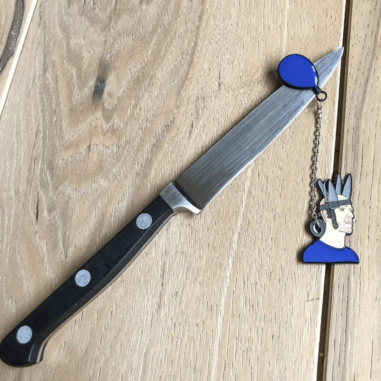 jan hakon erichson enamel pin with Jan wearing a blue shirt and  crown of duct taped knives with a blue balloon attatched to a chain goin through the duct tape roll.  the balloon of the pin is balanced on a kit hen knife. 