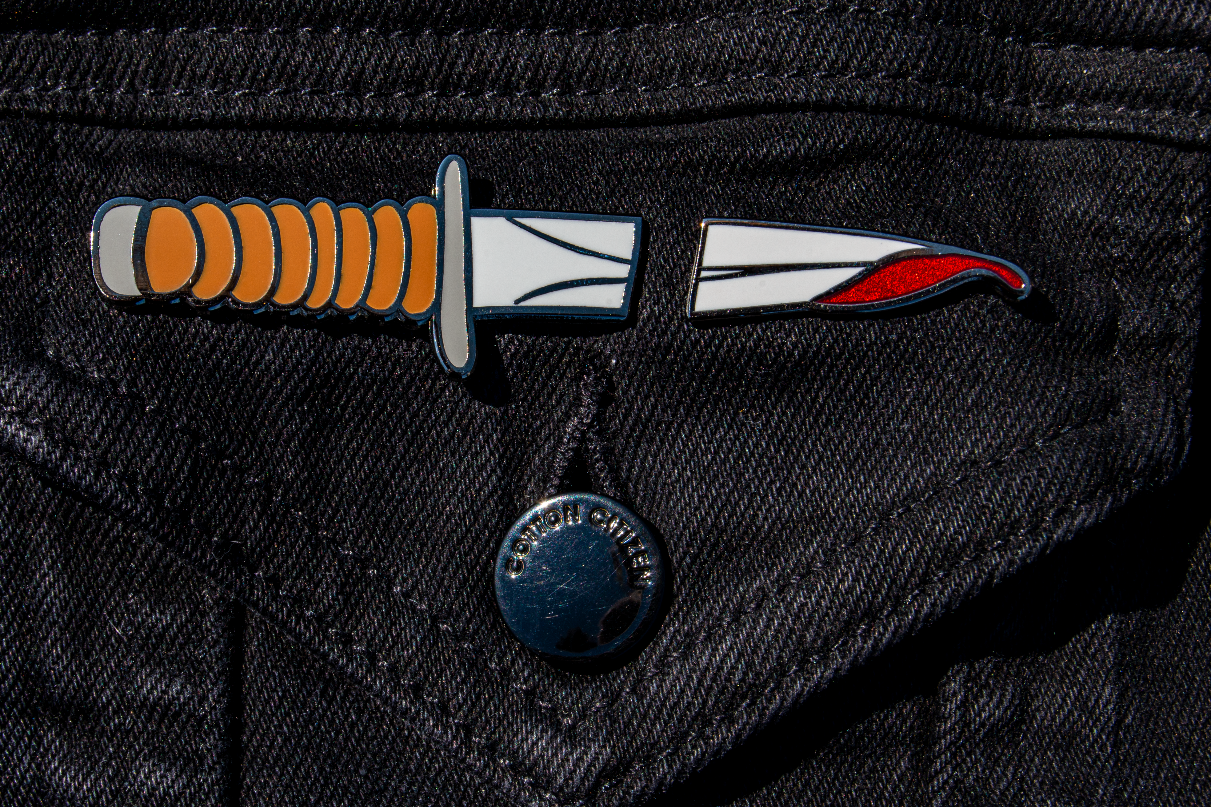 The knife pin set on a black denim jacket. With the split between the pins, it looks like a whole knife has gone through the fabric.