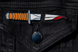 The knife pin set on a black denim jacket. With the split between the pins, it looks like a whole knife has gone through the fabric.