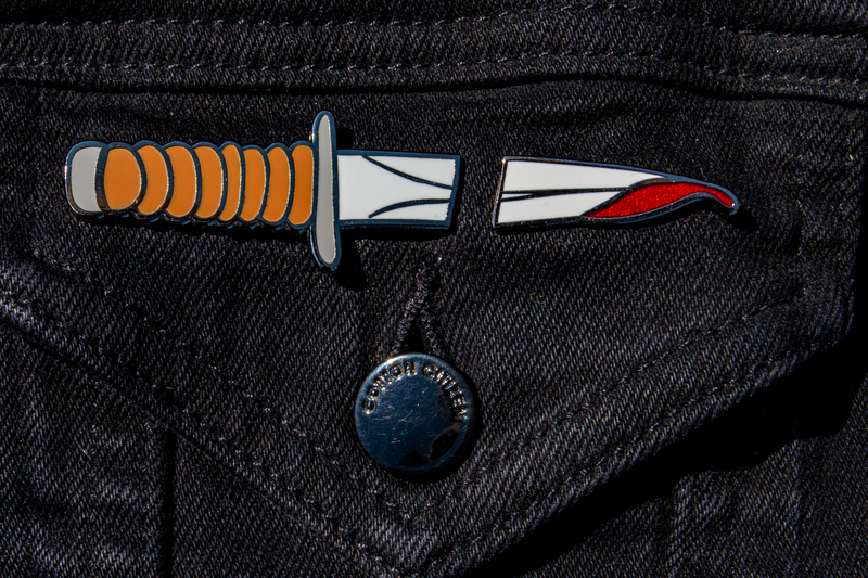 The knife pin set on a black denim jacket. With the split between the pins, it looks like a whole knife has gone through the fabric.