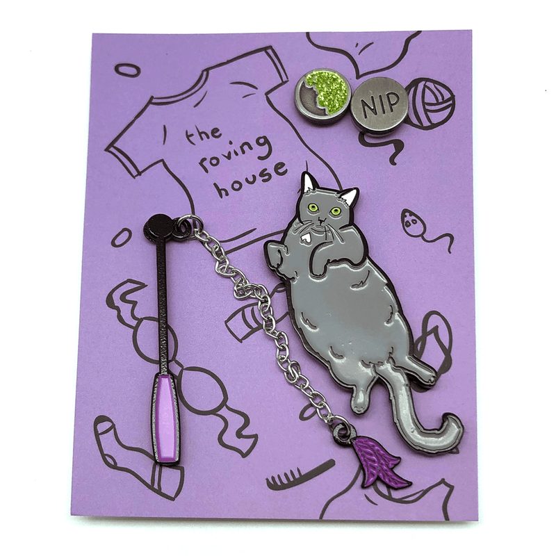 A pin set featuring a fat grey cat on her back, a dangling cat toy, and a tin of glitter catnip.