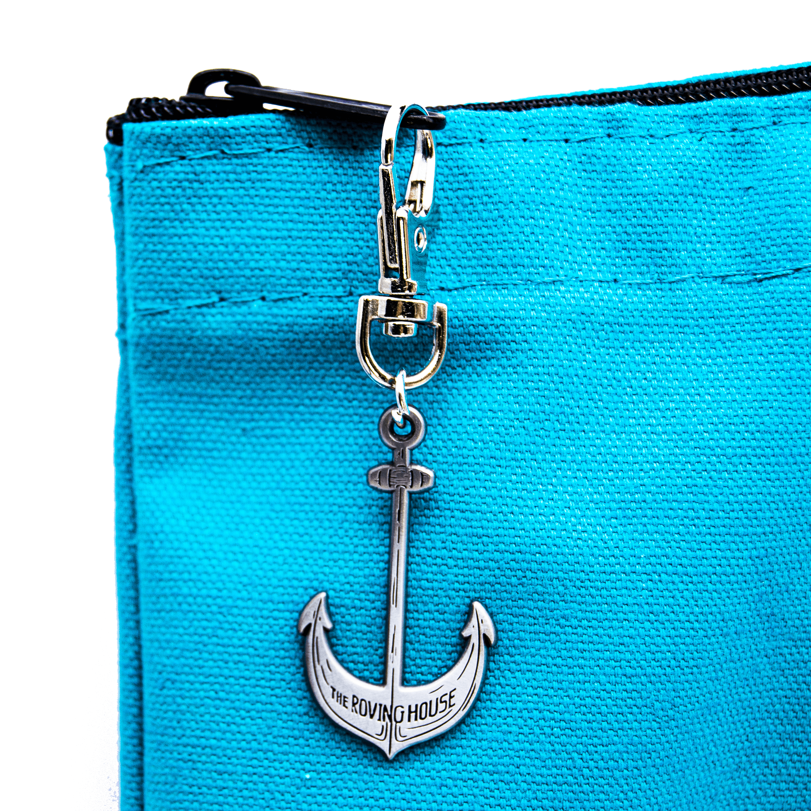 A close up of the ship's anchor shaped zipper pull on the turquoise tote bag. Small text on the anchor reads "The Roving House".